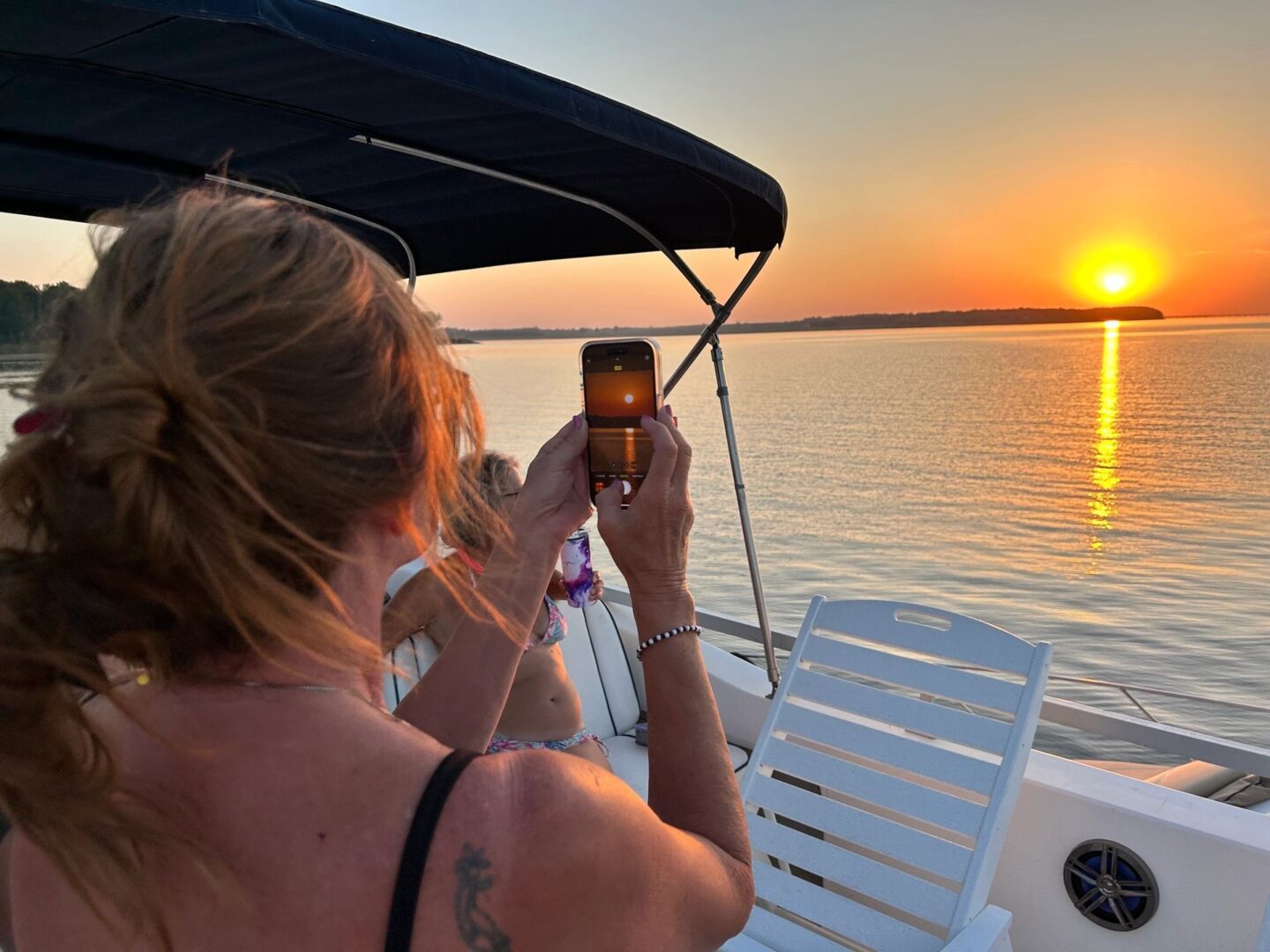 A woman taking a picture of the sunset on her phone.