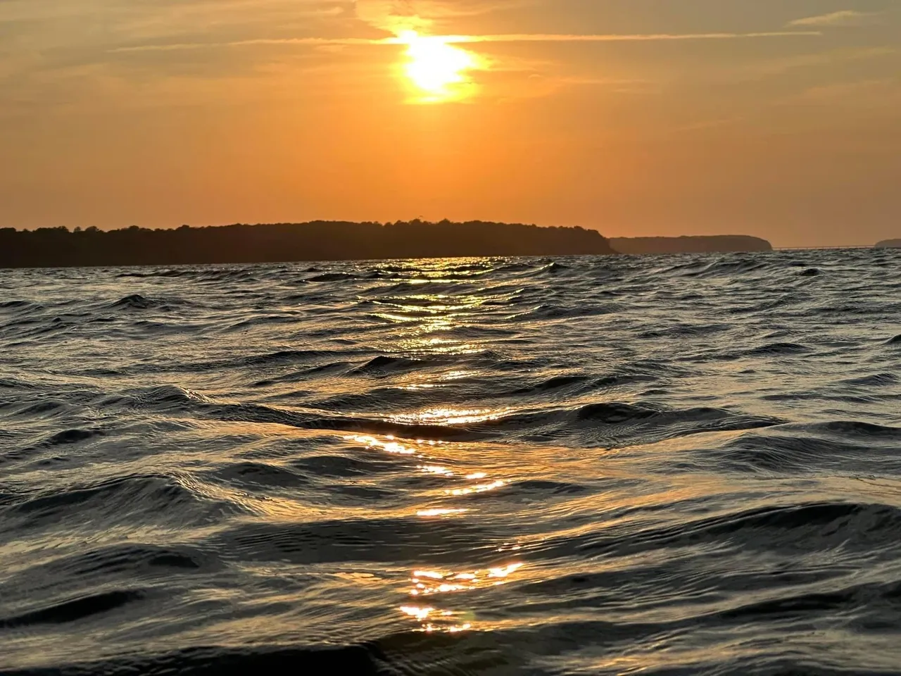 A sunset over the ocean with waves in front of it.