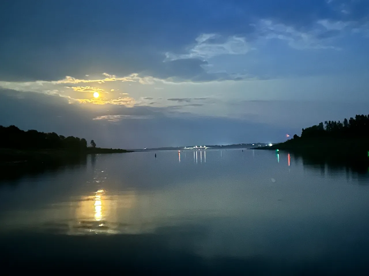 A body of water with the moon setting in the distance.